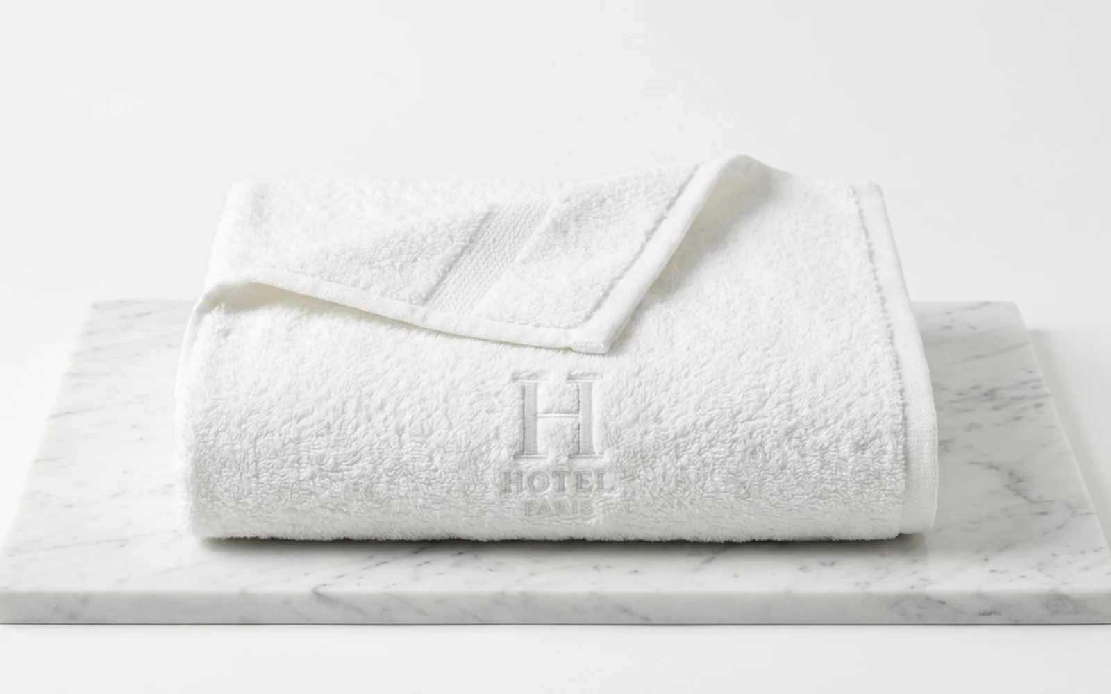 Serviette de bain blanche brodée d'une initiale sur la bande basse, posée sur du marbre