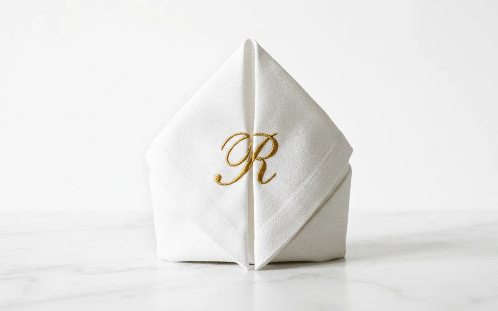 Serviette de table en lin pliée, monogramme brodé en fil or dans l'angle