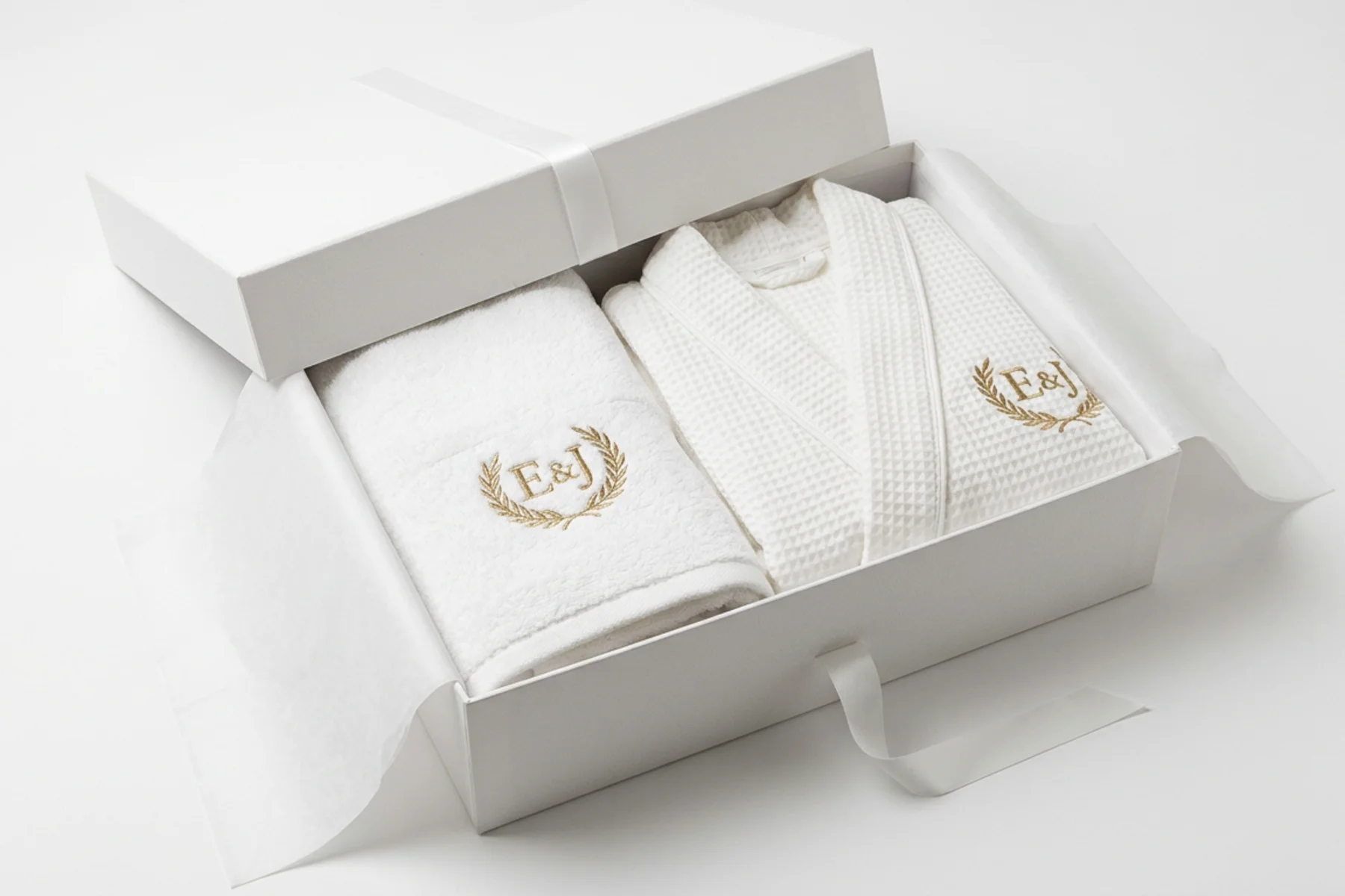 Devis serviette personnalisée : coffret cadeau ouvert contenant une serviette de bain et un peignoir en coton blanc brodés du monogramme E&J en fil doré