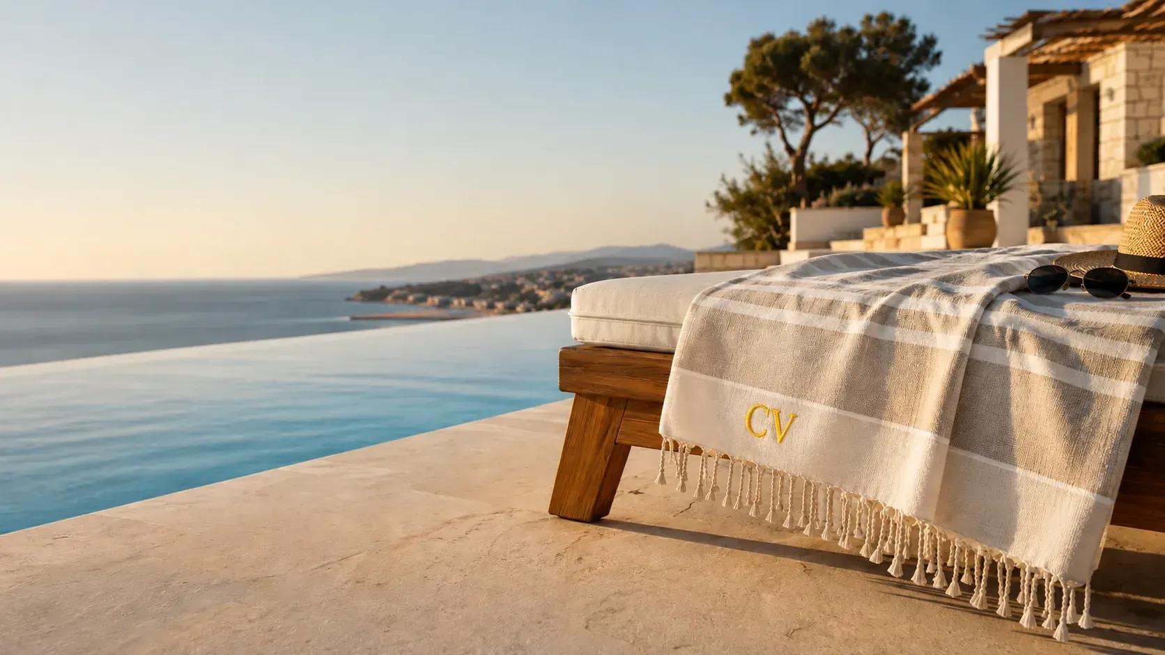 Fouta personnalisée rayée à franges, initiales CV brodées en fil doré, posée sur un transat face à la mer